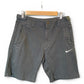 Dark gray Nike shorts with a white swoosh logo on the left leg, hanging from a wooden hanger against a white background.