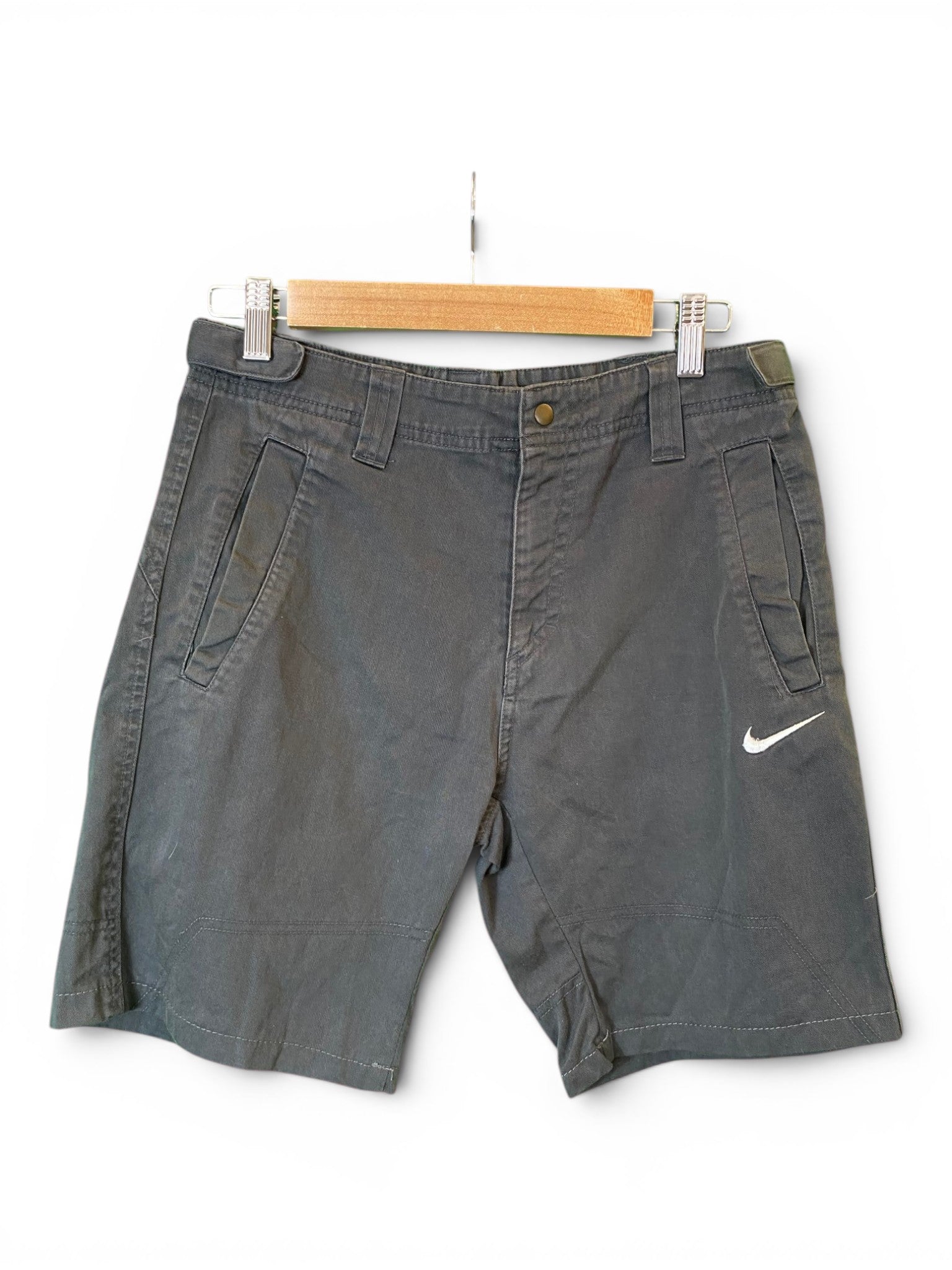 Dark gray Nike shorts with a white swoosh logo on the left leg, hanging from a wooden hanger against a white background.