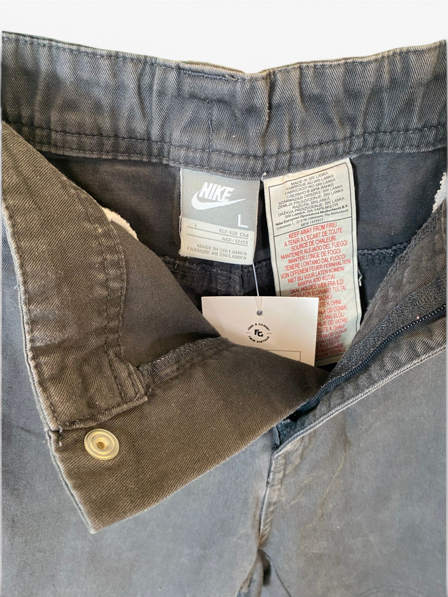 Close-up of the waistband and inner pocket area of a pair of Nike jeans, showing a faded gray denim fabric, interior labels, and a hangtag.