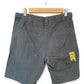 A pair of dark gray denim shorts hanging on a wooden hanger against a white background, showing the back pockets and a yellow Nike Swoosh logo patch on the right pocket.